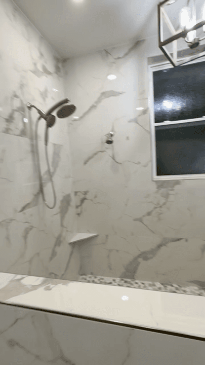Vertical video clip showing a bright marble-look shower and bathroom tile installation.