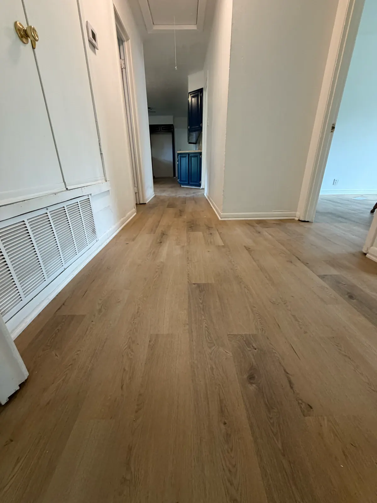 Wood-look plank flooring continuing through a hallway and doorways toward blue kitchen cabinets in a Pioneer Longview project