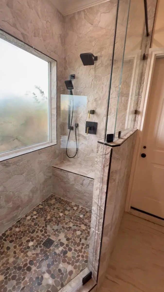 Finished shower with glass doors, a pony wall, veined tile, and black shower fittings