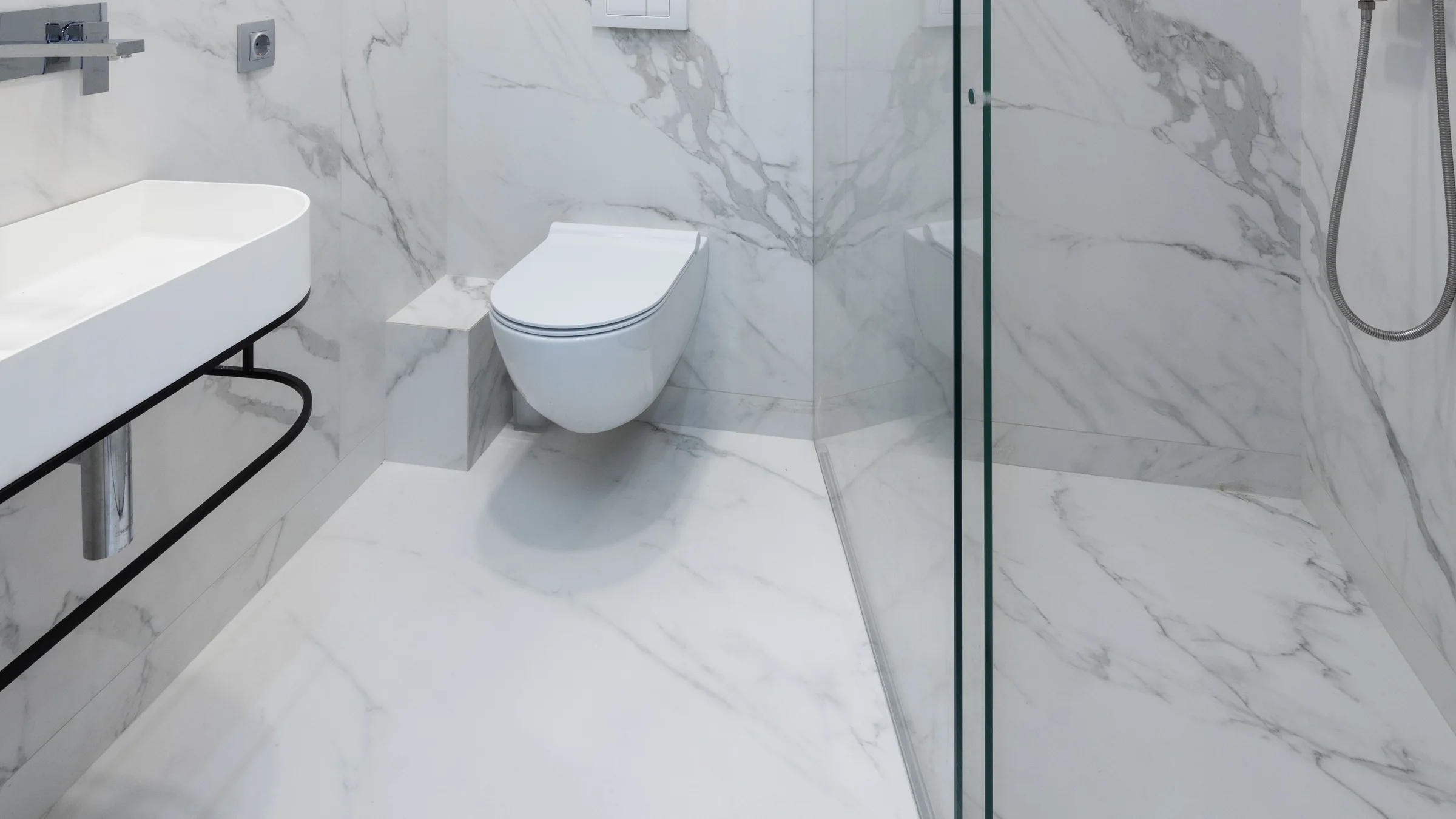 Representative zero-threshold shower with a flush marble-look floor transition, fixed glass panel, and linear drain