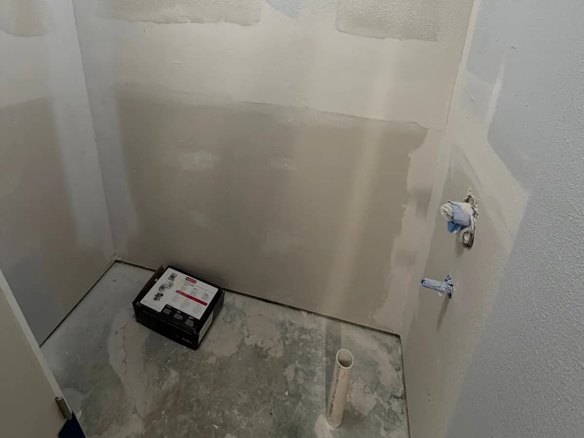 Exposed shower pan and prepared wall backing with drain opening and plumbing penetrations