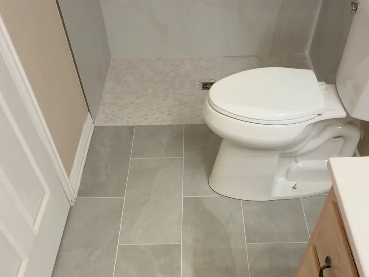 Small-format shower mosaic meeting larger bathroom floor tile without a raised curb