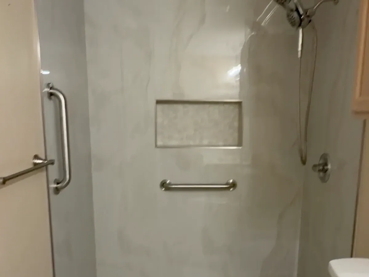 Finished shower with a recessed soap niche, horizontal grab bar, and handheld shower fixture