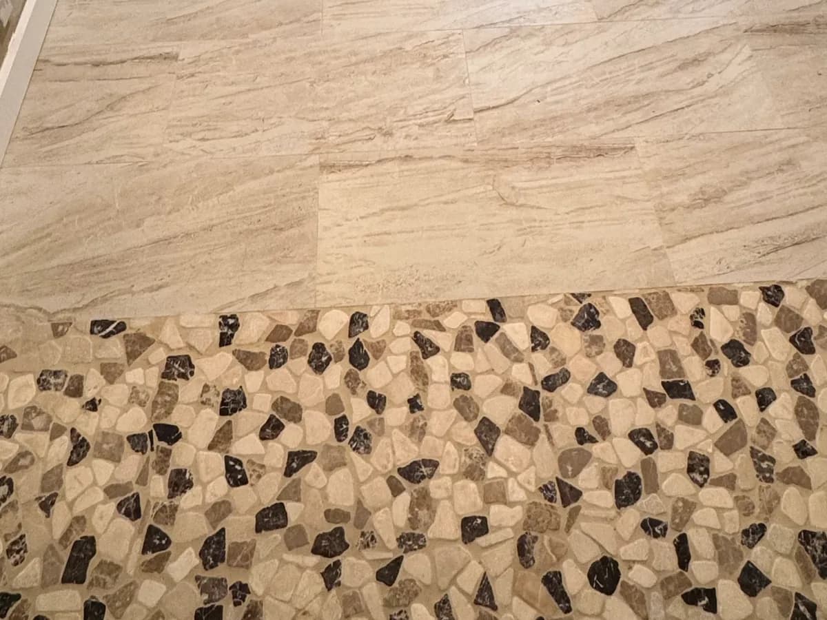 Light bathroom-floor tile meeting mixed-tone shower mosaic without a raised threshold