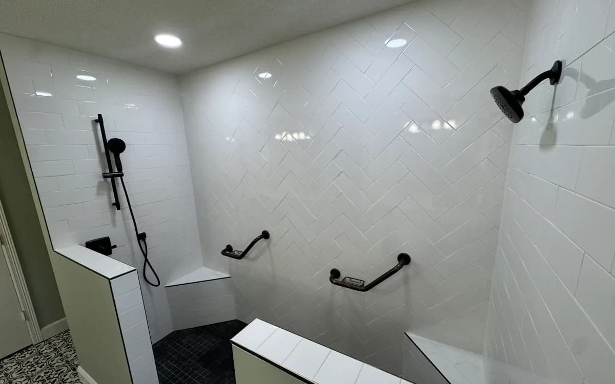 White herringbone shower feature wall beside horizontal tile, black fixtures, and grab bars