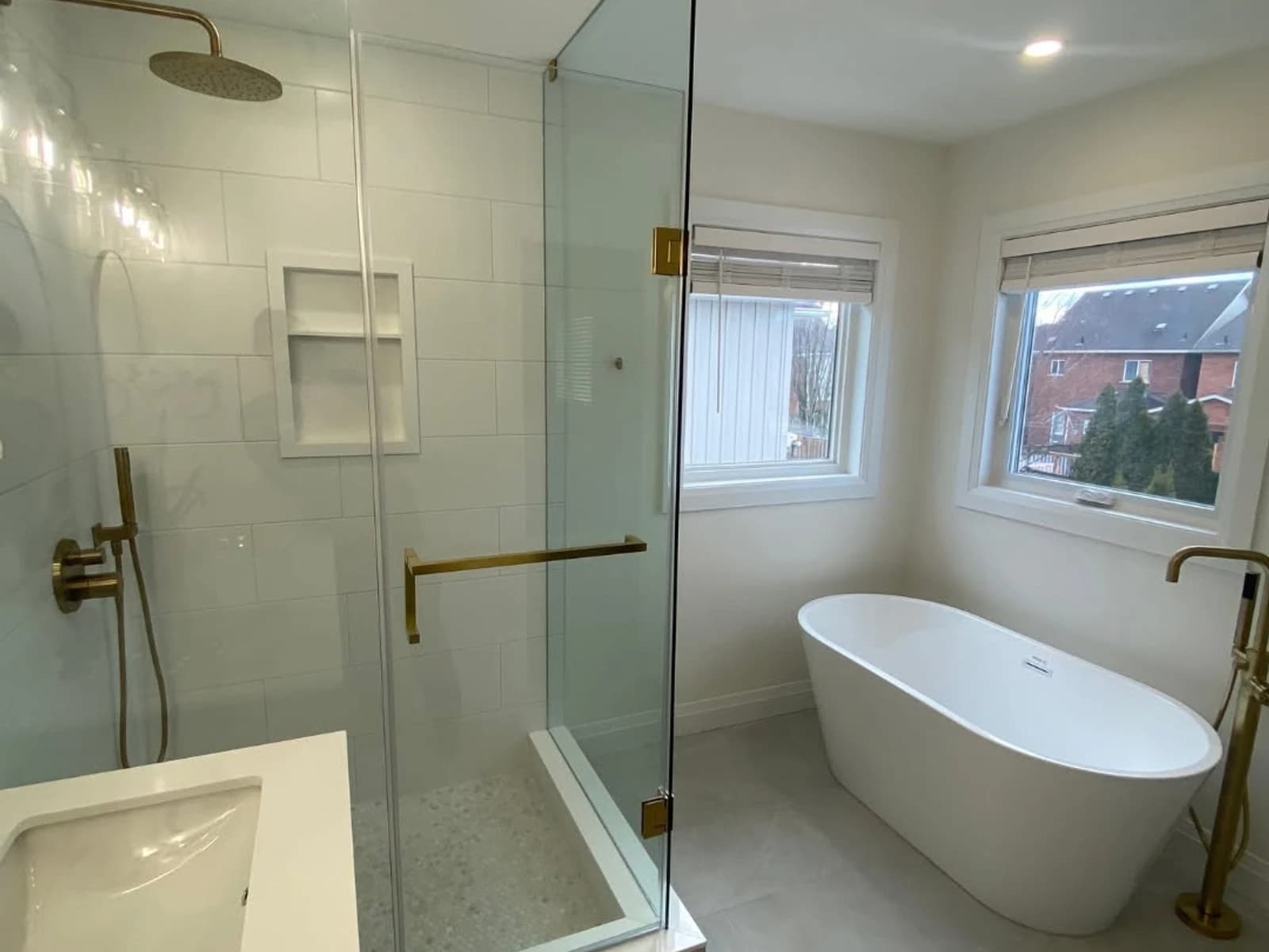 Bathroom remodel with freestanding tub, glass shower, white wall tile, window, and brass shower hardware