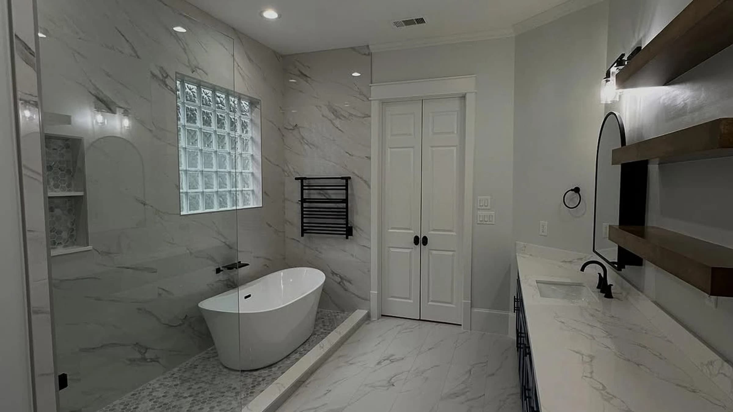 Bathroom remodel with marble-look tile, freestanding tub, glass shower, blue vanity, and glass block window