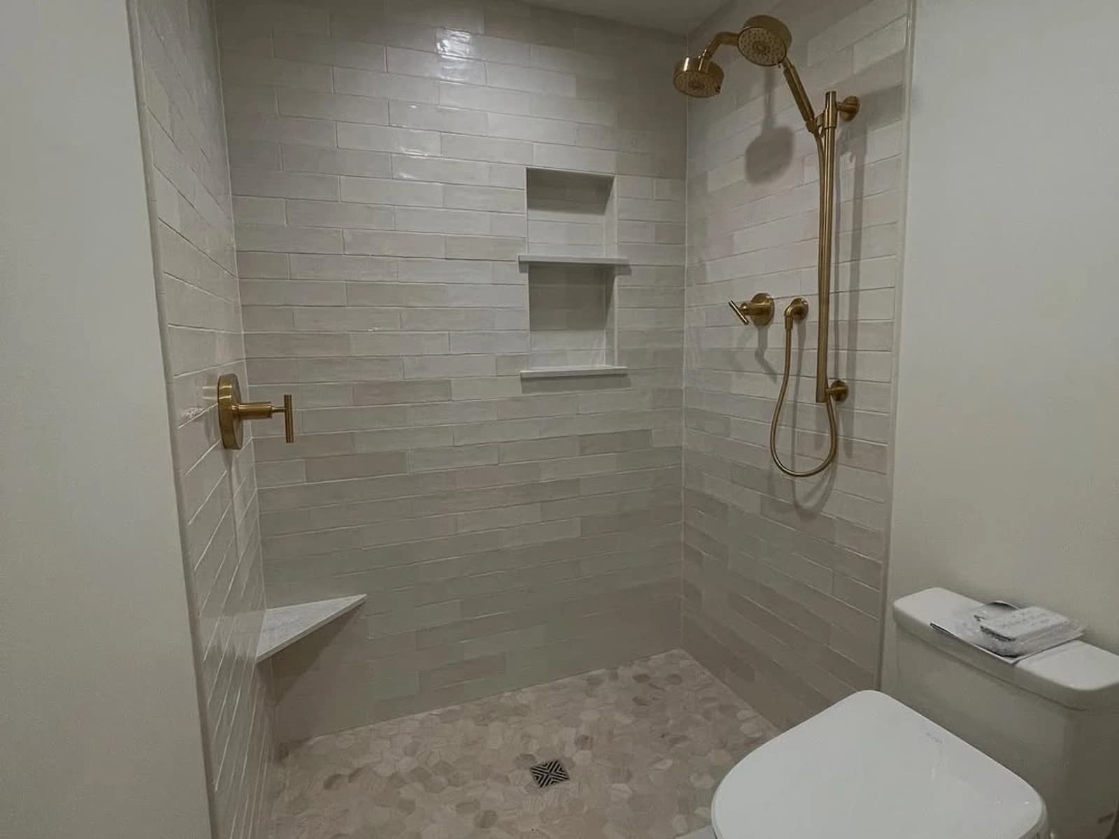 Walk-in shower with light tile walls, gold fixtures, a built-in niche, and a nearby toilet