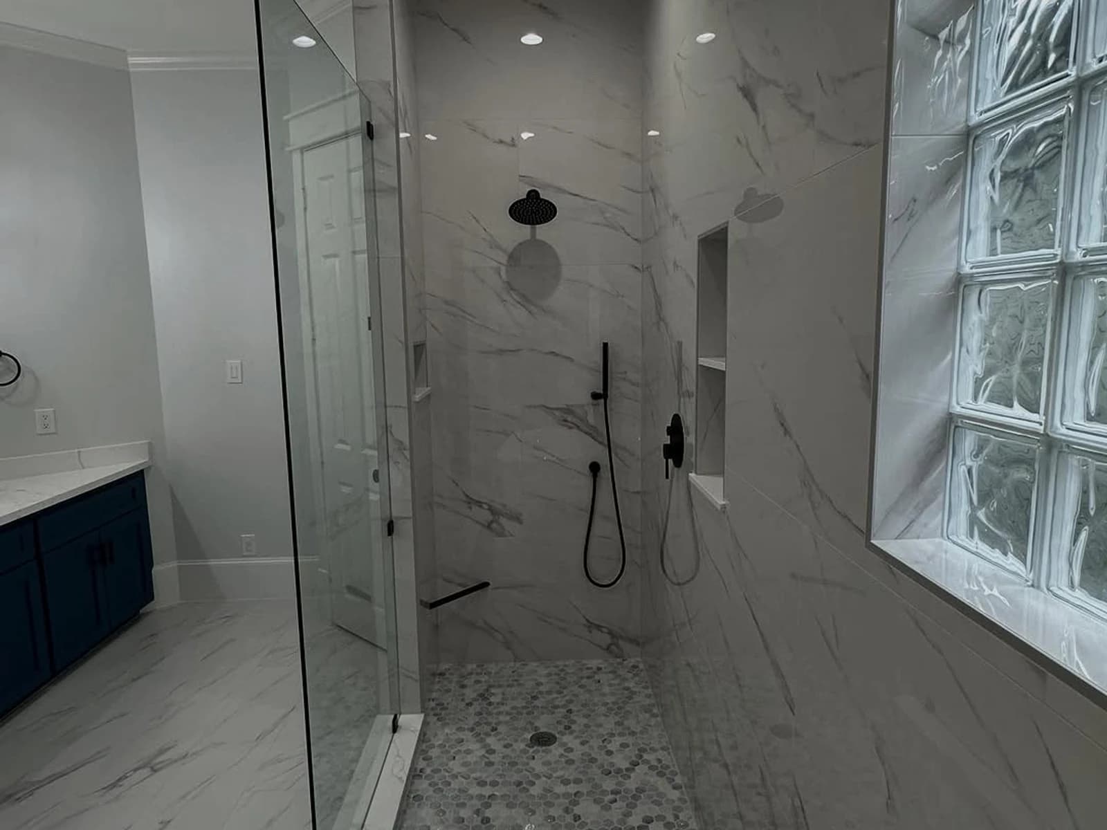 Walk-in shower tile installation with glass panels, marble-look tile, built-in niche, and black hardware