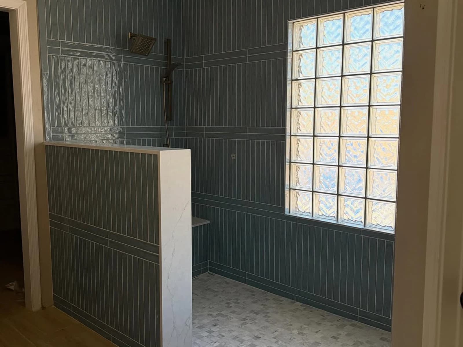 Walk-in shower with vertical blue-green wall tile, a low divider, window glass, and gold fixtures