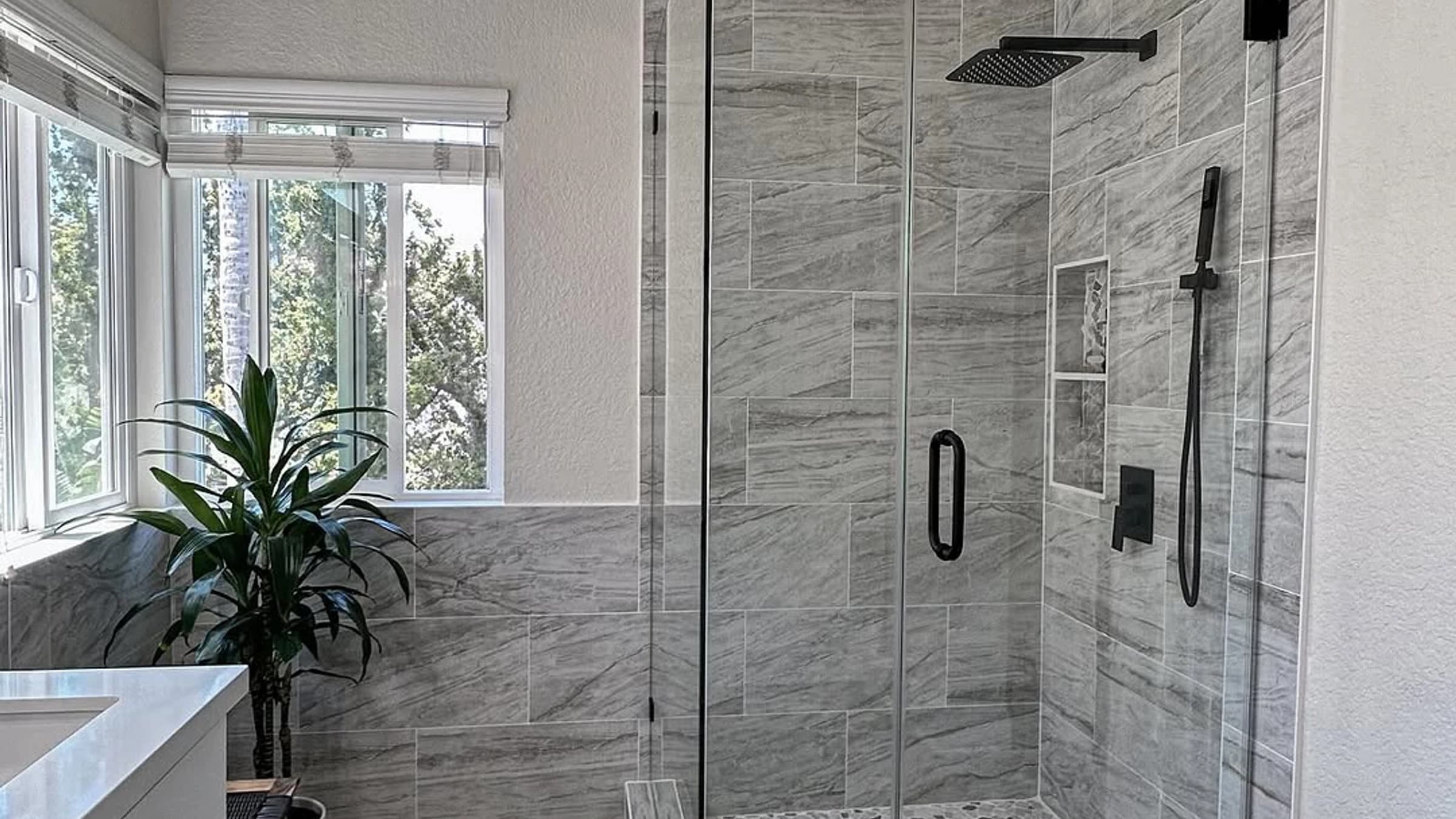 Finished custom shower with gray wall tile, glass enclosure, wood-look floor, and natural light