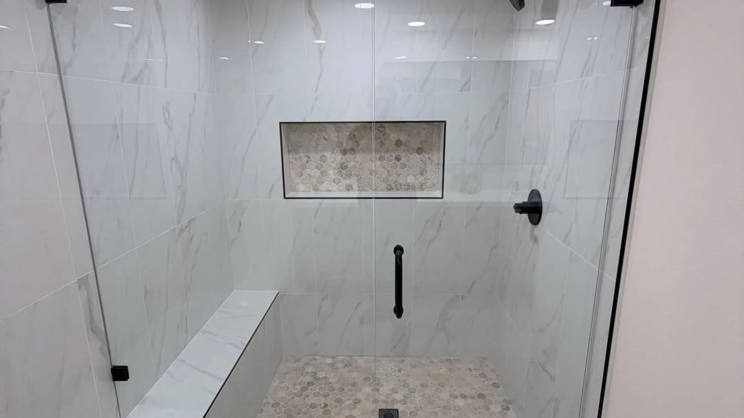 Glass-enclosed shower with marble-look wall tile, black hardware, a bench, and a recessed niche