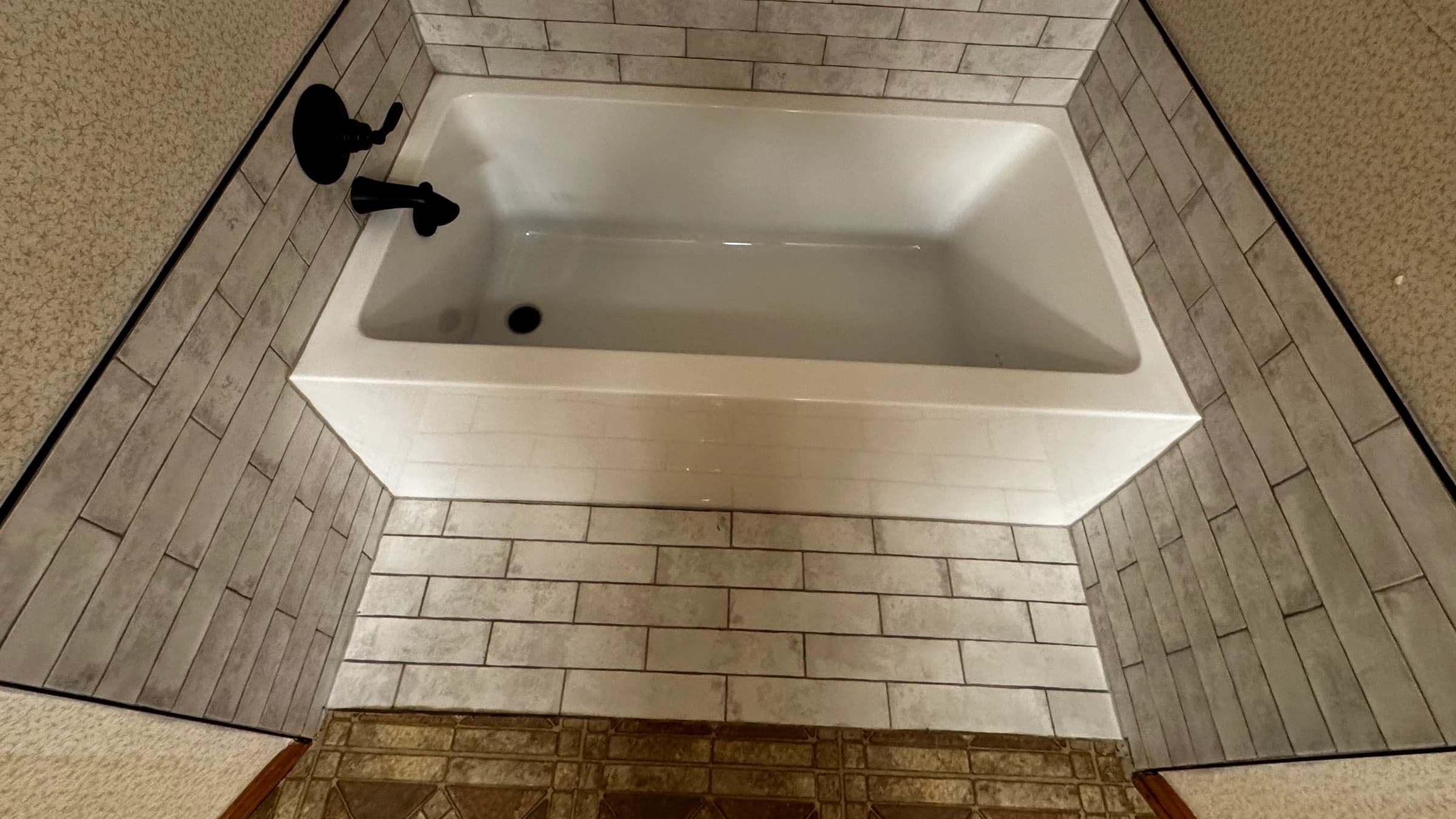 New white bathtub with light rectangular tile, dark edge trim, and black tub hardware in Flint TX