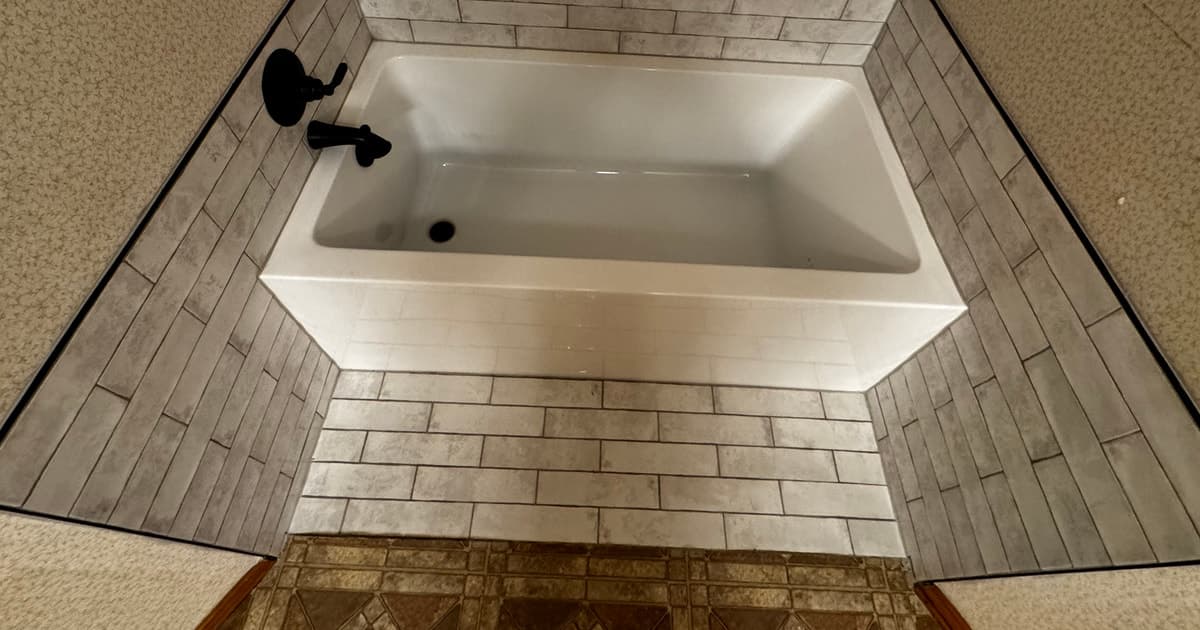 New white bathtub with light rectangular tile, dark edge trim, and black tub hardware in Flint TX