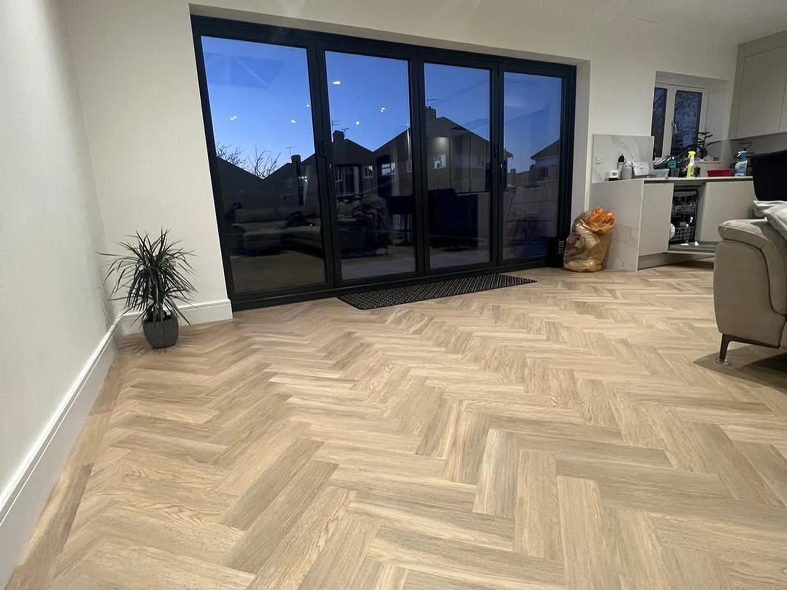 Living room with light herringbone wood-look flooring, black patio doors, recessed lights, and pale walls