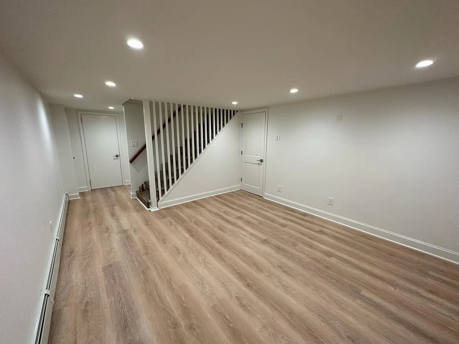 Light wood-look plank flooring across an open room beside a staircase and white walls