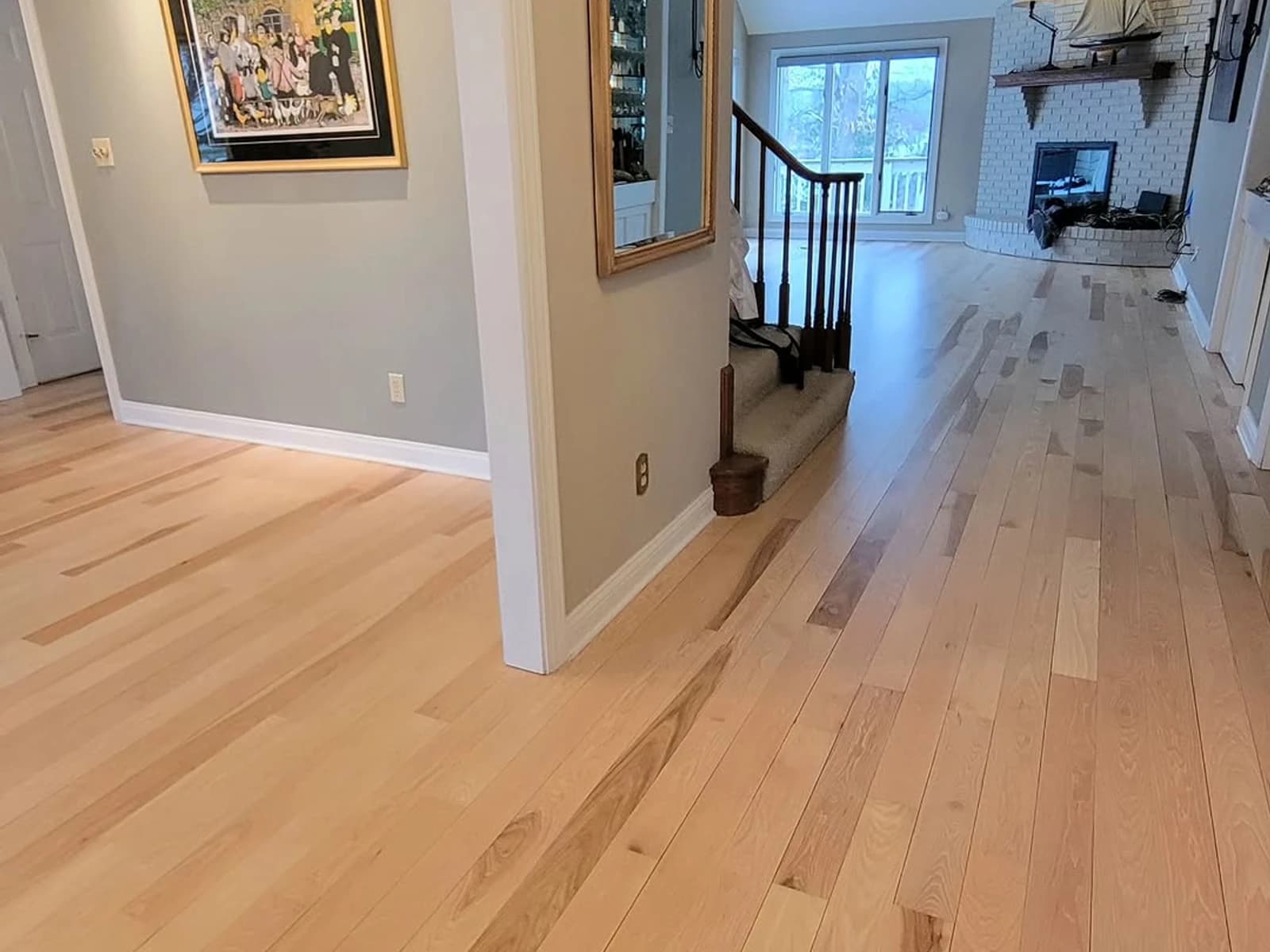 Light wood flooring through a hallway and living area with white trim and a staircase opening