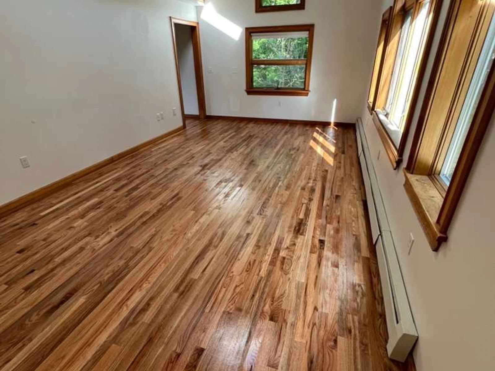 Finished hardwood flooring installation with tall wood-trim windows, white walls, and natural light