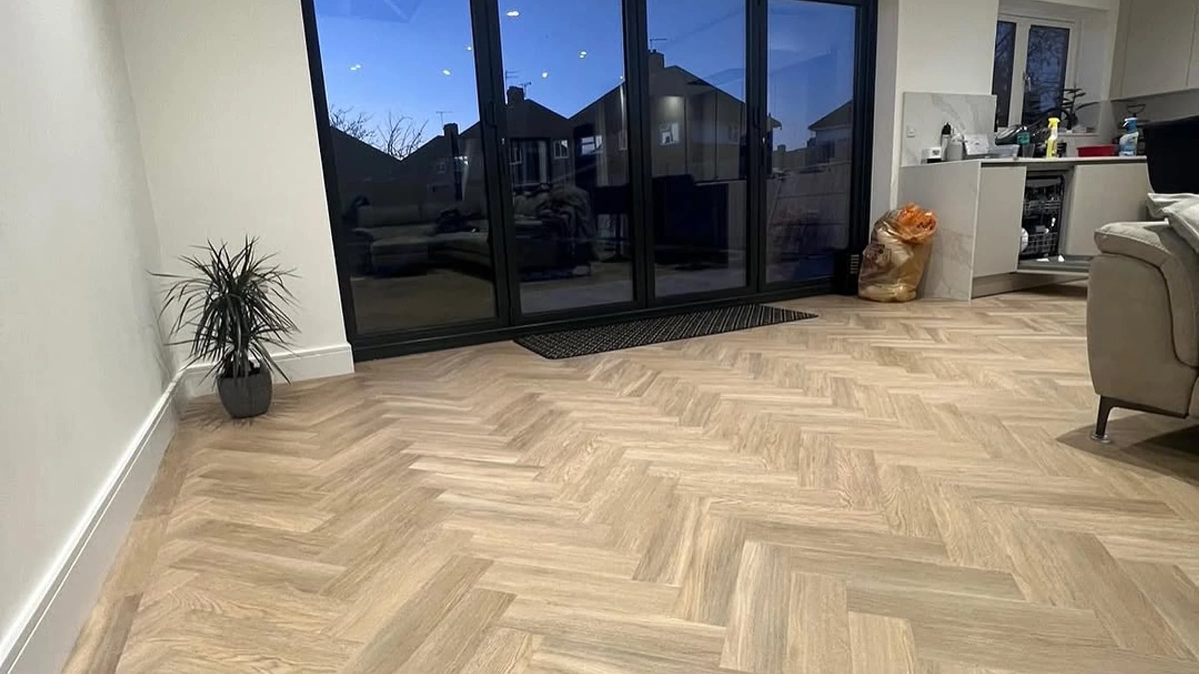 Living room with light herringbone wood-look flooring, black patio doors, recessed lights, and pale walls