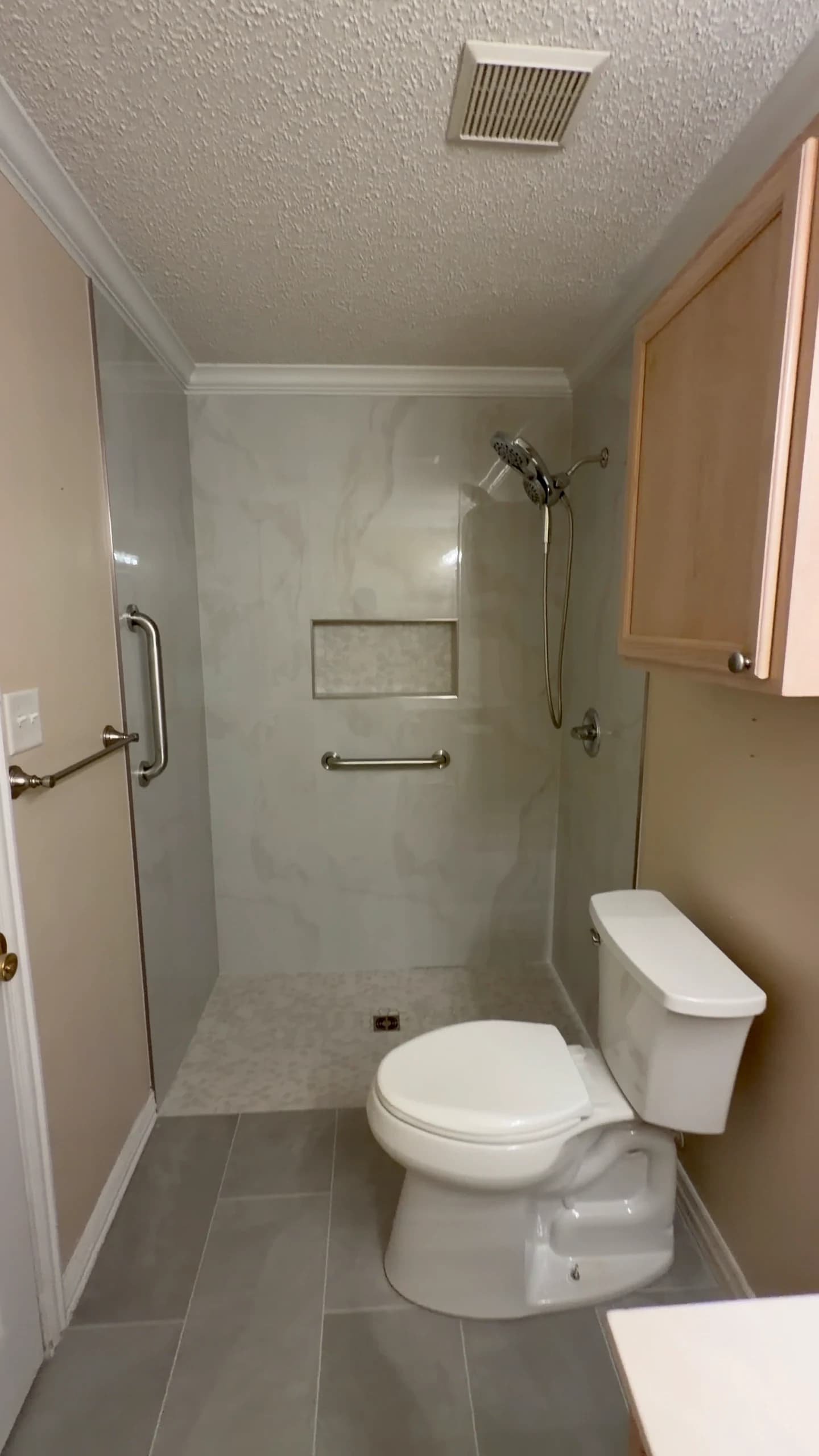 Finished walk-in shower with grab bars, recessed soap niche, and mosaic shower floor