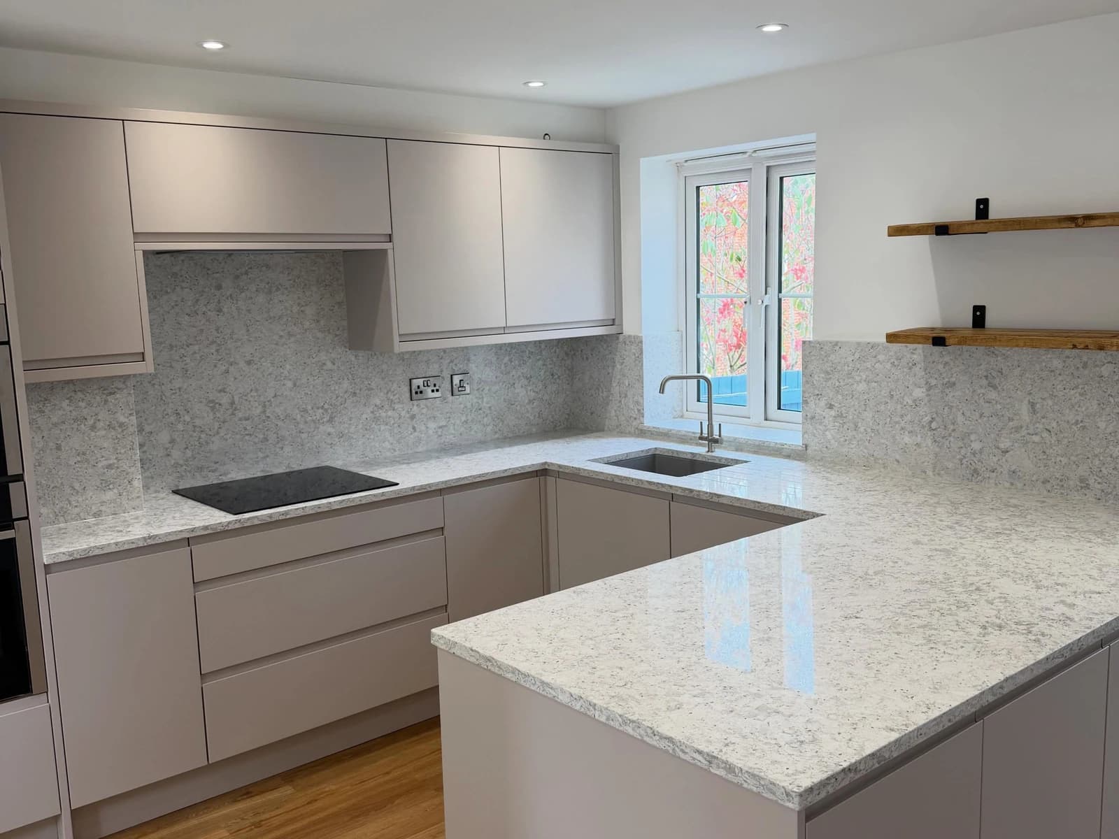 Kitchen sink wall with green shaker cabinets, brass faucet, white counter, and wood-look flooring