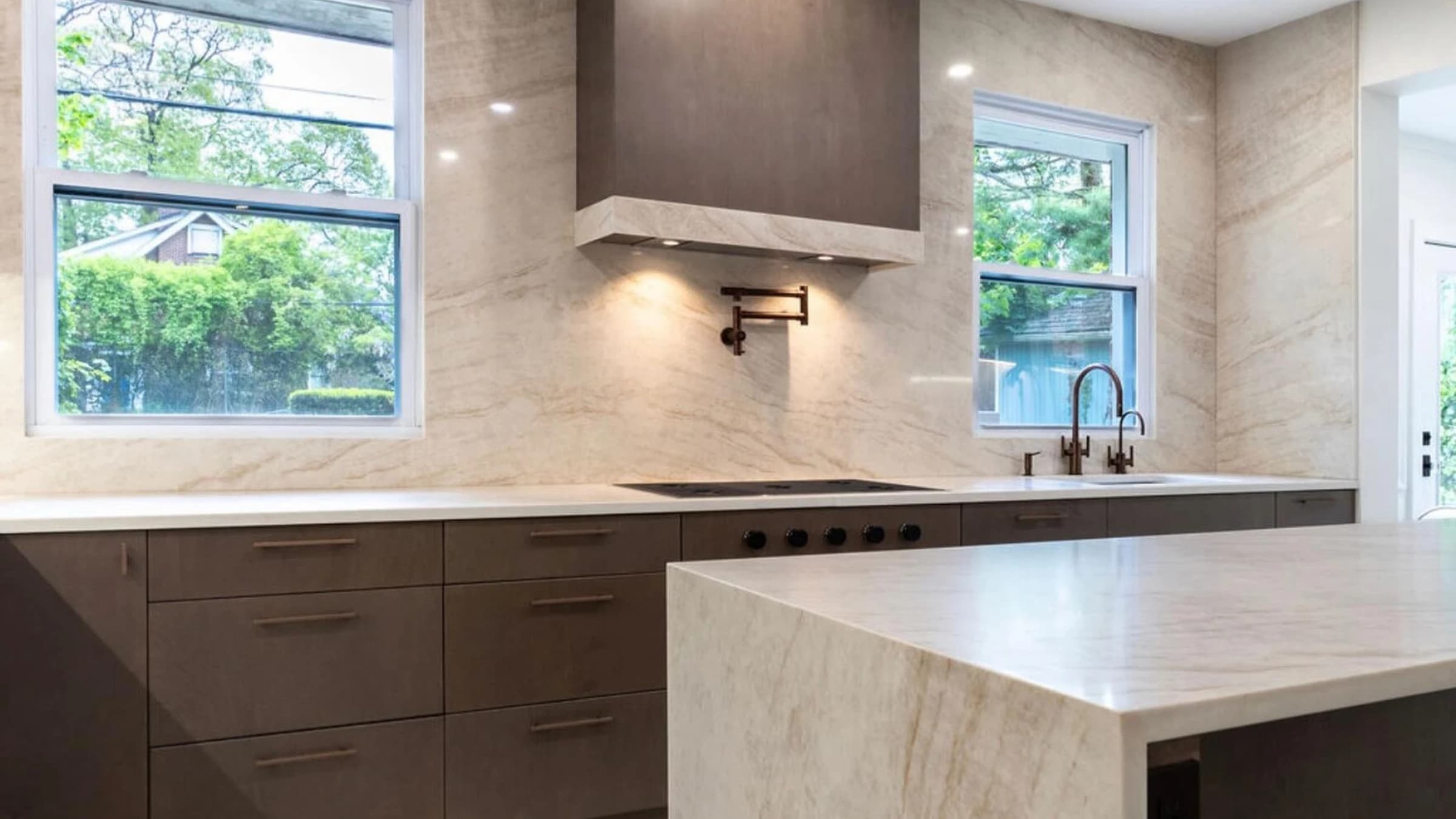 Modern kitchen remodel with flat-panel cabinets, waterfall island, marble-look backsplash, recessed lighting, and large windows