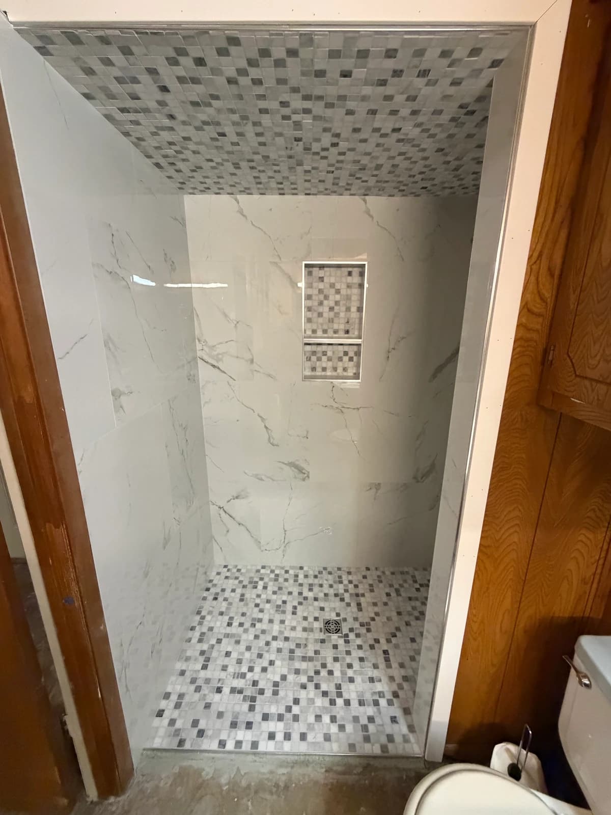 Curbless shower entrance with marble-look walls, gray-and-white mosaic floor and ceiling, and a recessed niche