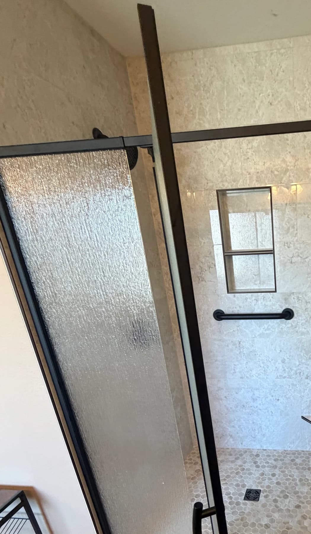 Finished custom tile shower with black-framed glass door, recessed niche, grab bar, mosaic floor, and black shower hardware